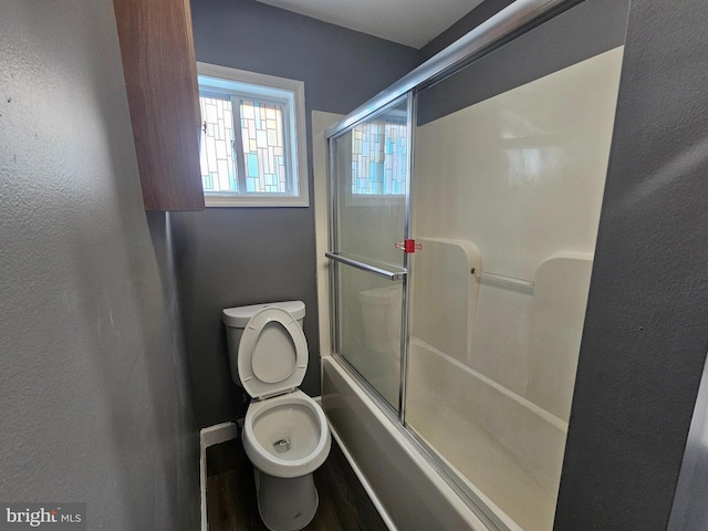 full bathroom featuring toilet, baseboards, a textured wall, and shower / bath combination with glass door
