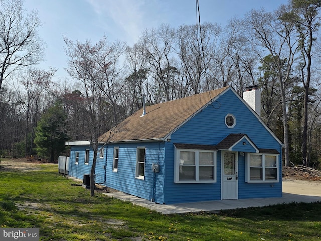 exterior space with central air condition unit, a chimney, a shingled roof, and a front yard