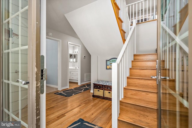 staircase with vaulted ceiling, wood finished floors, visible vents, and baseboards