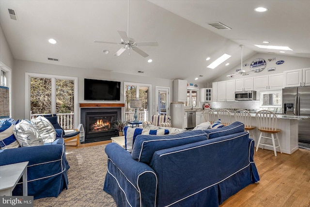 living area featuring light wood-type flooring, visible vents, and vaulted ceiling with skylight