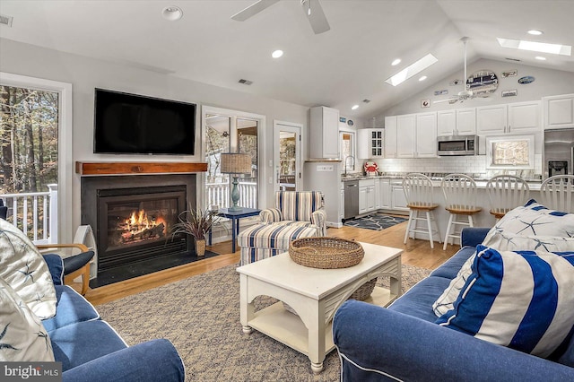 living area with light wood-type flooring, a ceiling fan, lofted ceiling with skylight, and a fireplace with flush hearth