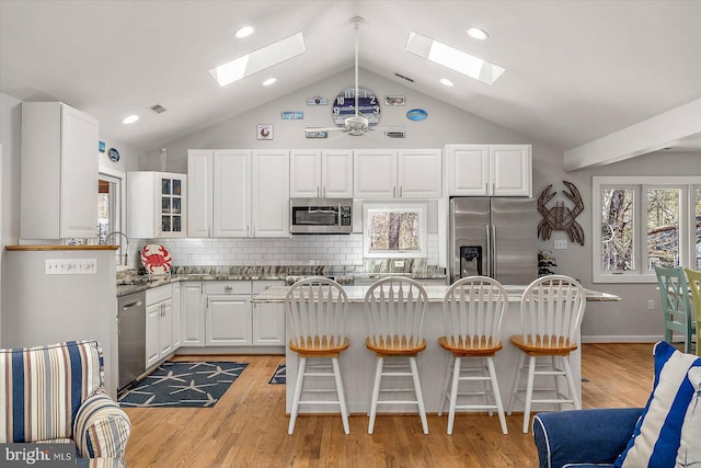 kitchen with white cabinets, a skylight, stainless steel appliances, and a sink
