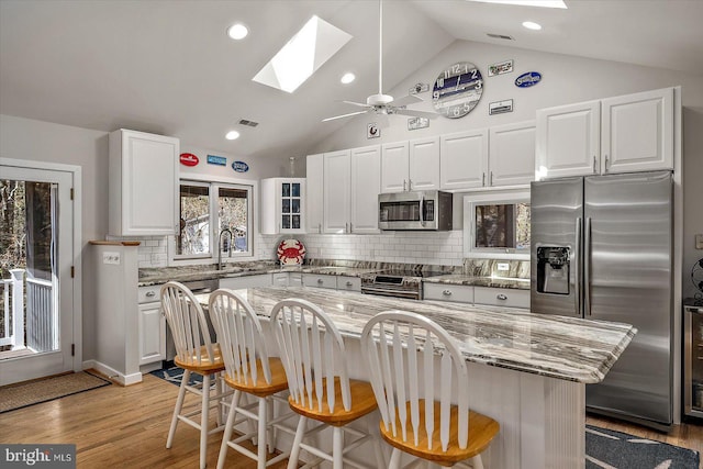 kitchen with vaulted ceiling with skylight, a sink, stainless steel appliances, a kitchen bar, and white cabinetry