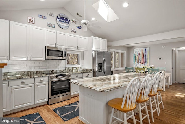 kitchen with a skylight, stainless steel appliances, a center island, and white cabinetry