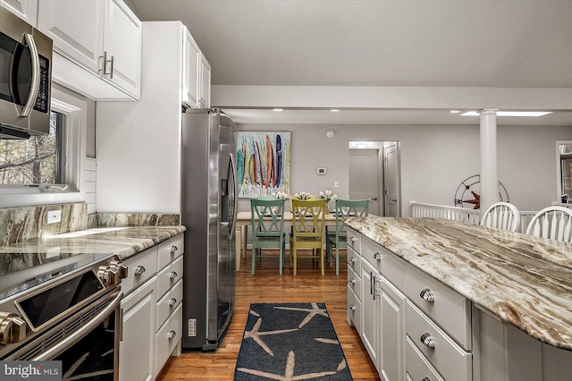 kitchen featuring white cabinets, light stone counters, stainless steel appliances, and light wood-style flooring