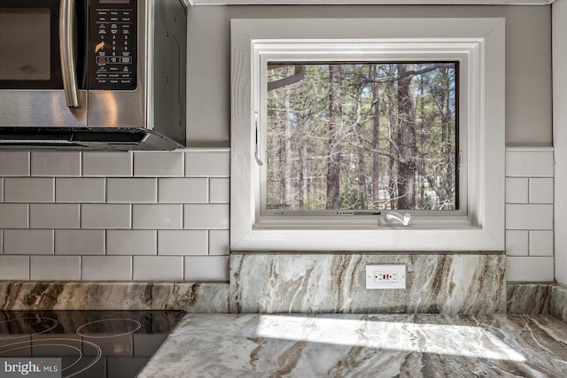 interior details with stainless steel microwave, stovetop, tasteful backsplash, and light stone countertops
