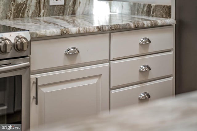 details featuring electric range, white cabinetry, light stone counters, and oven