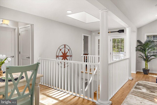 corridor with an upstairs landing, a skylight, light wood-style floors, baseboards, and decorative columns