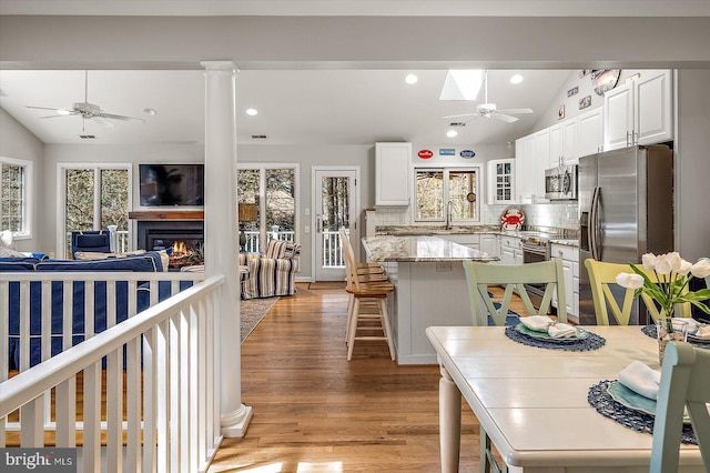 kitchen featuring a ceiling fan, vaulted ceiling with skylight, decorative backsplash, light wood-style floors, and stainless steel appliances