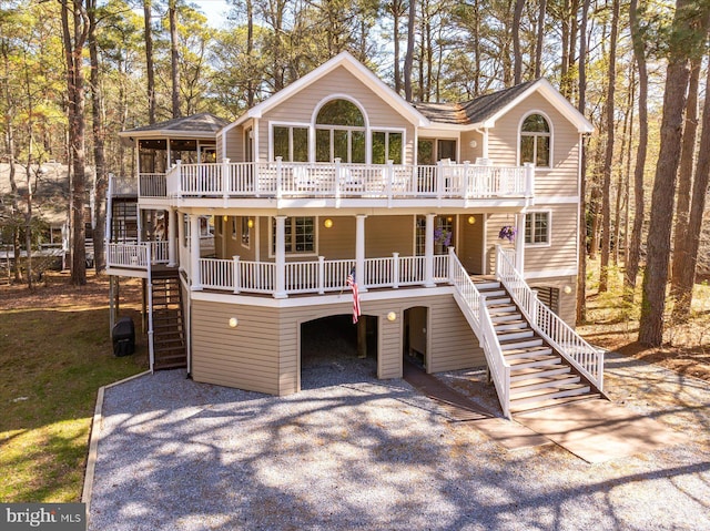 view of front facade featuring a carport, covered porch, a wooden deck, stairs, and gravel driveway