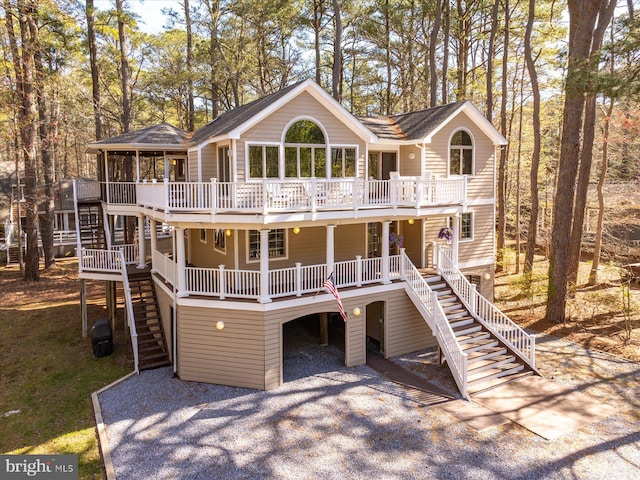 view of front facade with roof with shingles, a porch, stairs, a deck, and gravel driveway