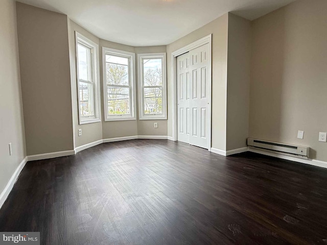 unfurnished bedroom featuring a baseboard heating unit, baseboards, dark wood-type flooring, and a closet