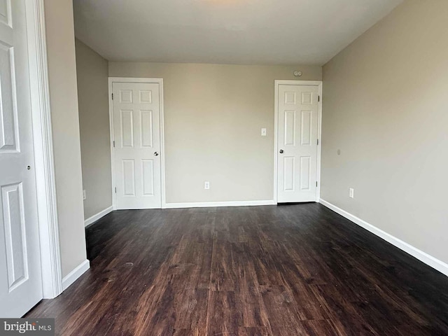 unfurnished bedroom with baseboards and dark wood-style floors