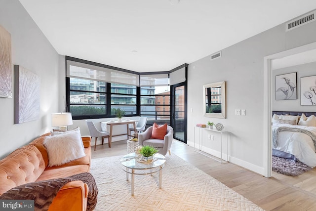 living area with floor to ceiling windows, wood finished floors, visible vents, and baseboards