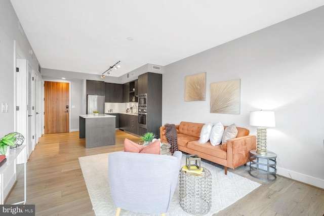 living area with baseboards, track lighting, visible vents, and light wood-style floors