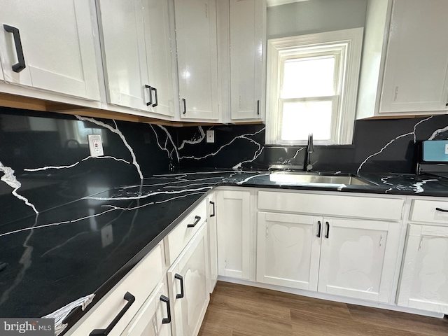 kitchen with white cabinets, dark countertops, wood finished floors, and a sink