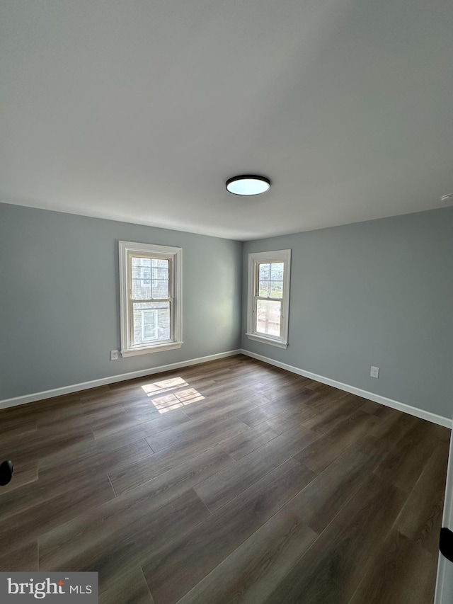 empty room featuring baseboards and dark wood-type flooring