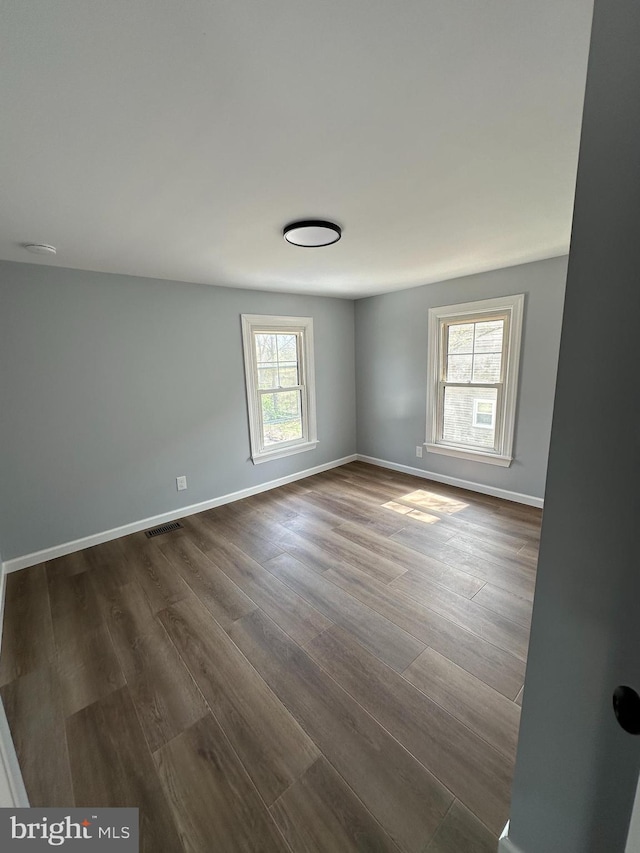 spare room featuring baseboards, dark wood-style flooring, and visible vents