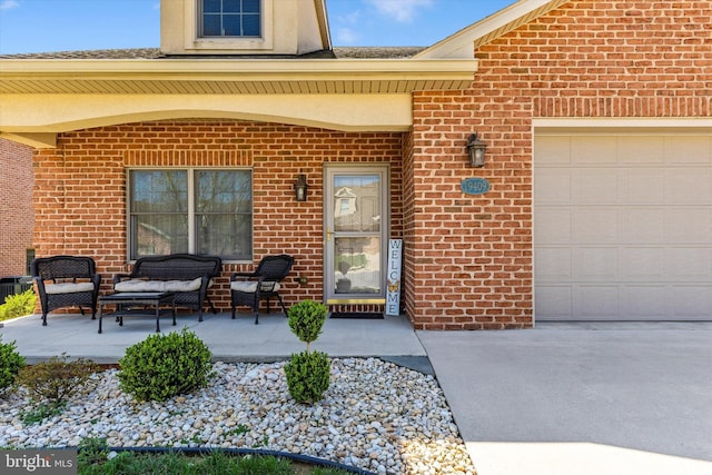 doorway to property featuring brick siding, driveway, covered porch, and a garage