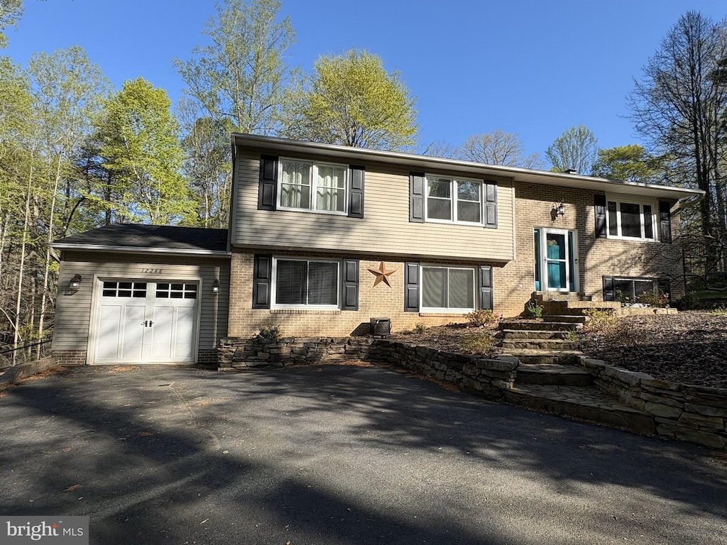 split foyer home featuring brick siding, an attached garage, and aphalt driveway