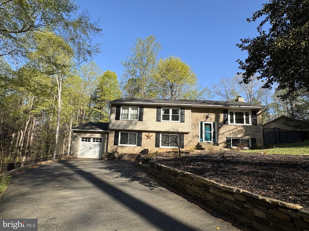 bi-level home with a chimney, a garage, aphalt driveway, and brick siding