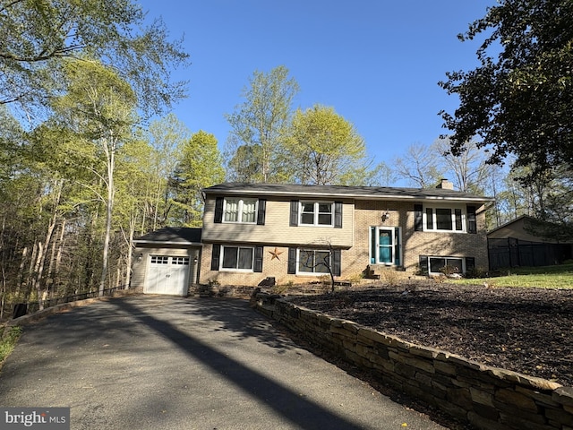bi-level home with a chimney, a garage, aphalt driveway, and brick siding