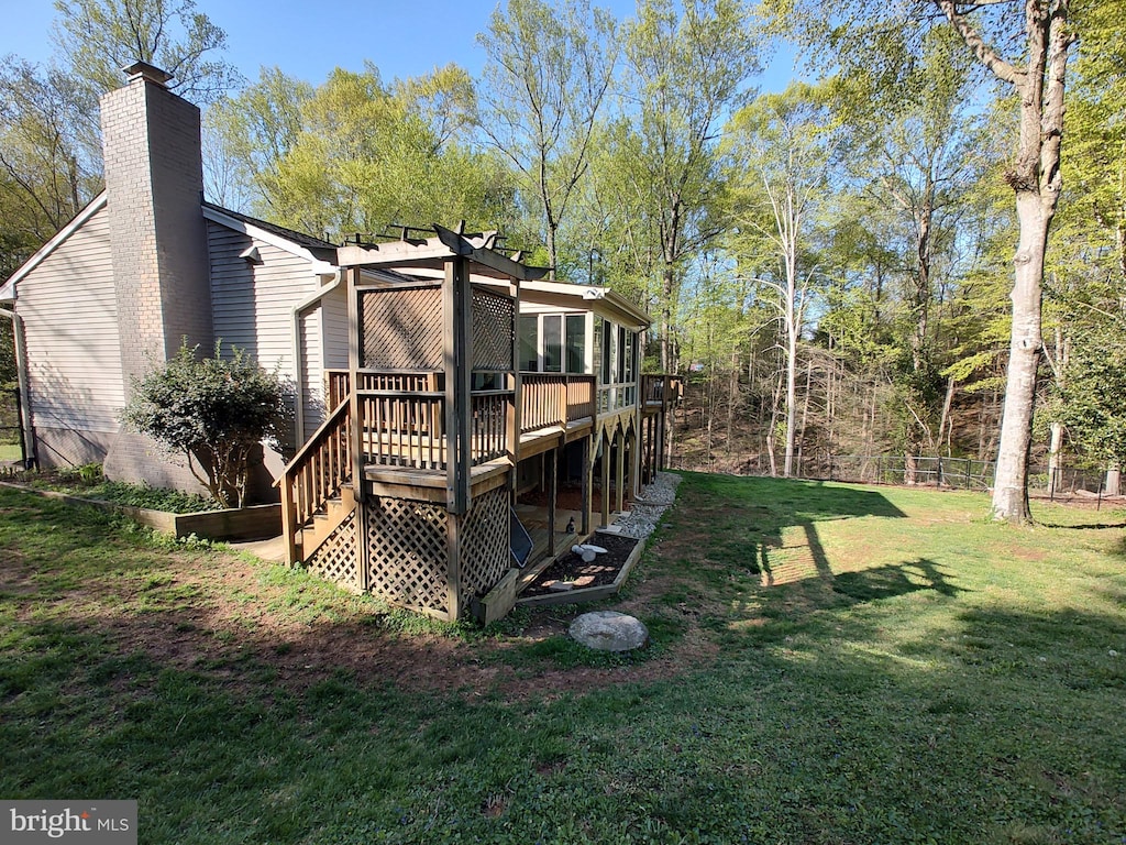 rear view of property with a chimney, fence, a deck, and a lawn