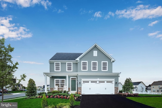 traditional-style home with covered porch, aphalt driveway, an attached garage, stone siding, and a front yard