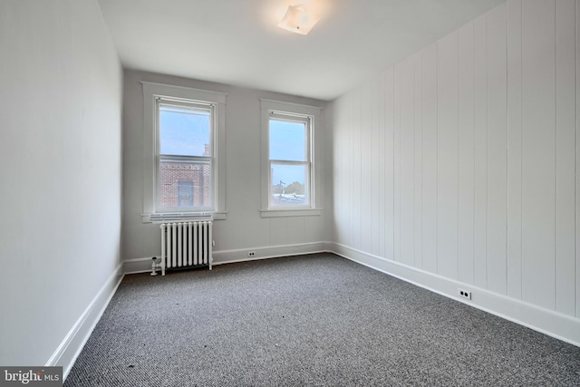 empty room featuring radiator heating unit, dark colored carpet, and baseboards