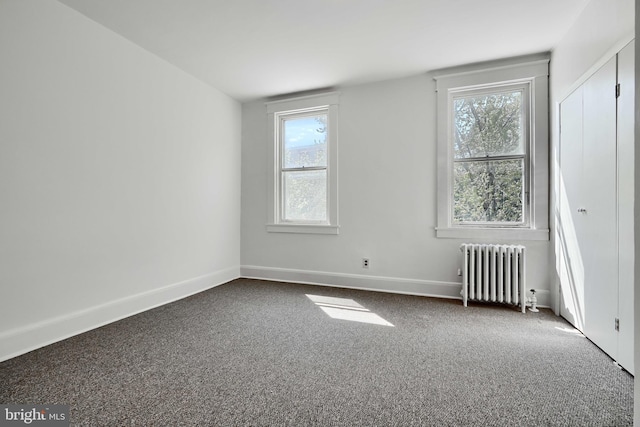 empty room featuring dark carpet, radiator heating unit, and a wealth of natural light