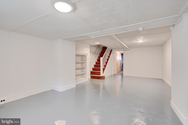 finished below grade area featuring stairway, baseboards, and built in shelves
