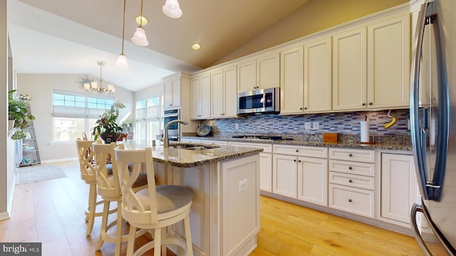 kitchen with lofted ceiling, light wood finished floors, stainless steel appliances, backsplash, and stone counters