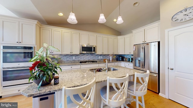 kitchen with a sink, light wood-style floors, lofted ceiling, decorative backsplash, and appliances with stainless steel finishes