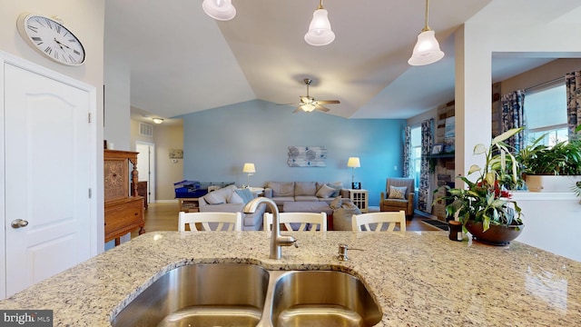 kitchen featuring lofted ceiling, a ceiling fan, a sink, light stone countertops, and hanging light fixtures
