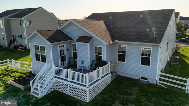 back of house at dusk featuring central AC, fence, a lawn, a shingled roof, and a deck