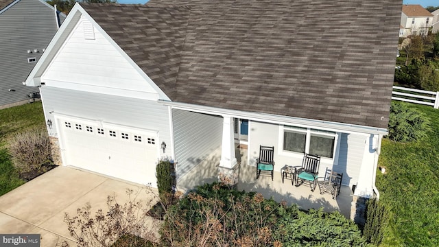 view of front of house featuring a porch, a shingled roof, concrete driveway, and fence