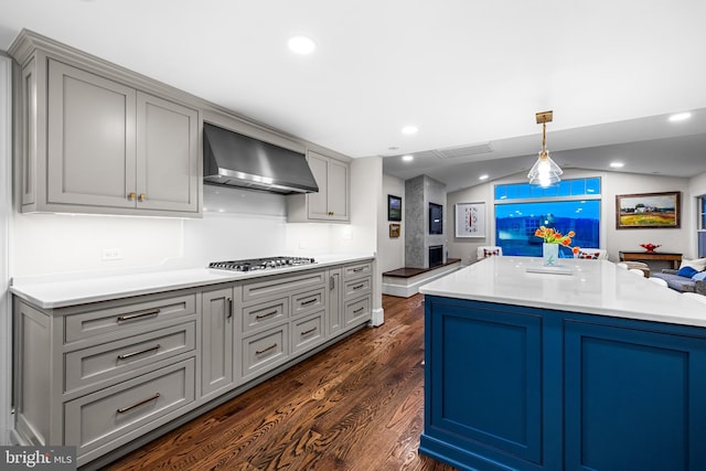 kitchen featuring gray cabinets, light countertops, wall chimney exhaust hood, dark wood finished floors, and stainless steel gas stovetop