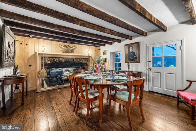 dining space featuring dark wood-type flooring, wooden walls, a fireplace, and beam ceiling
