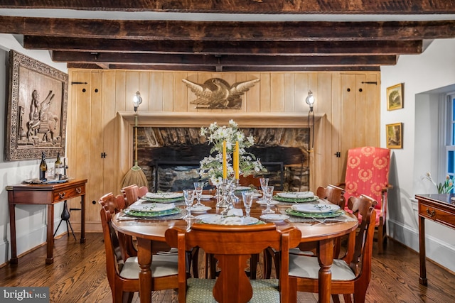 dining room featuring a stone fireplace, beam ceiling, baseboards, and wood finished floors