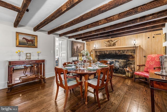 dining area featuring a stone fireplace, beam ceiling, baseboards, and wood-type flooring