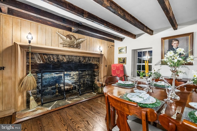dining room with wooden walls, beam ceiling, wood finished floors, and a fireplace
