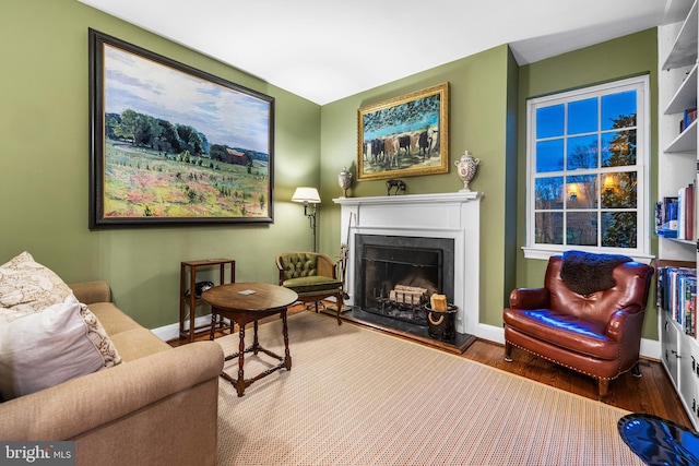 sitting room featuring wood finished floors, baseboards, and a fireplace with raised hearth