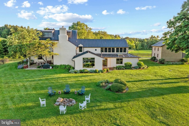 back of property with a chimney, a standing seam roof, a yard, metal roof, and fence