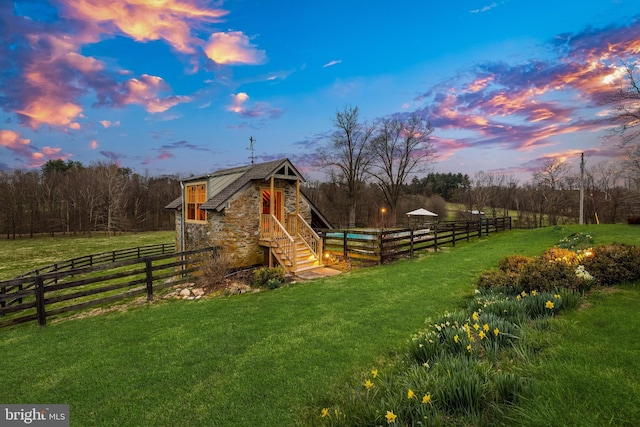 playground at dusk with a rural view, a yard, and fence
