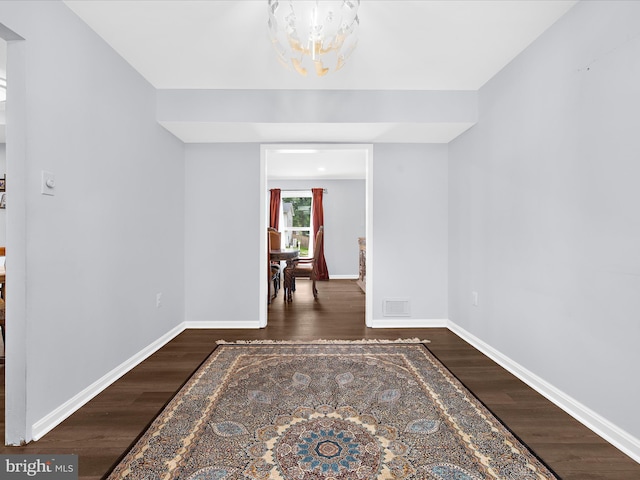 empty room featuring a chandelier, wood finished floors, and baseboards