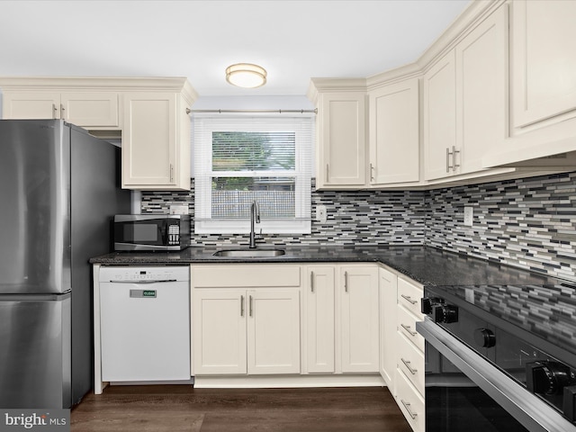 kitchen featuring stainless steel appliances, a sink, backsplash, dark wood-style flooring, and dark stone countertops