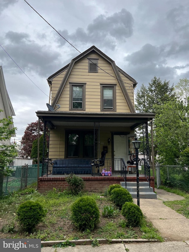 dutch colonial featuring a porch, a gambrel roof, and fence