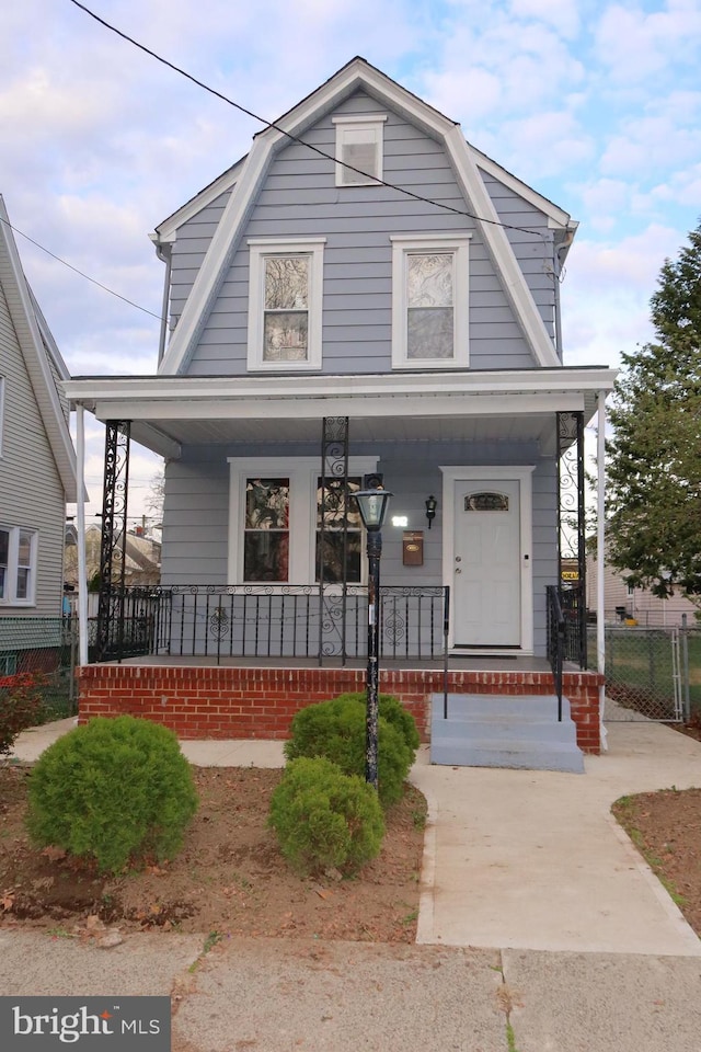 colonial inspired home featuring fence, a gambrel roof, and covered porch