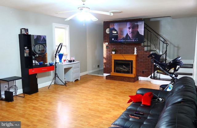 living room with wood finished floors, baseboards, a ceiling fan, and a brick fireplace