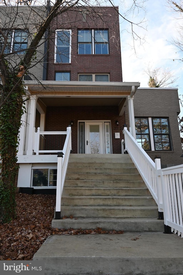 view of front of home featuring a porch, stairway, and brick siding